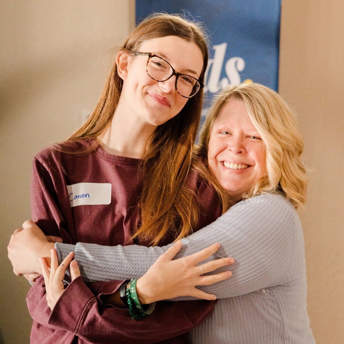 Two friends hugging and smiling, one wearing a name tag.