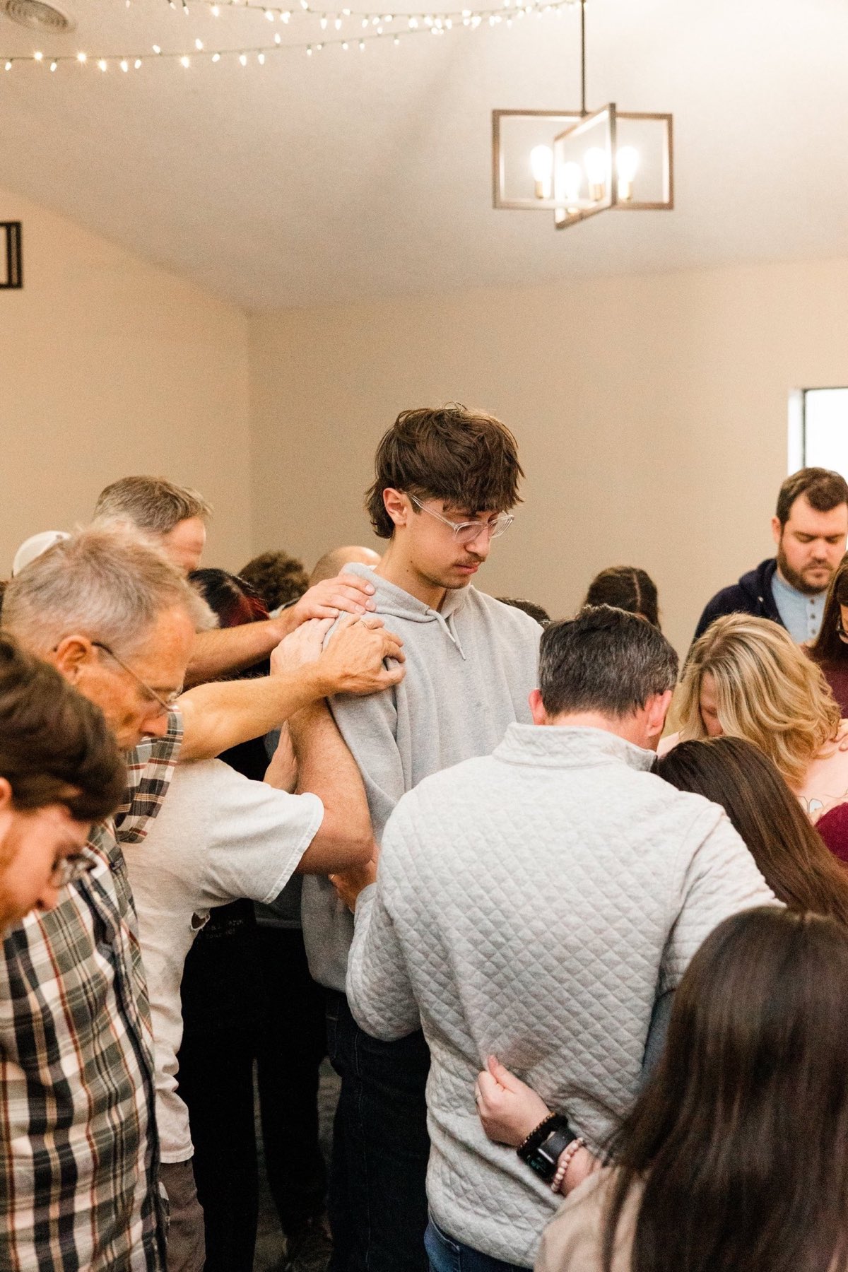 Church members gathered in a circle praying with hands on one another's shoulders
