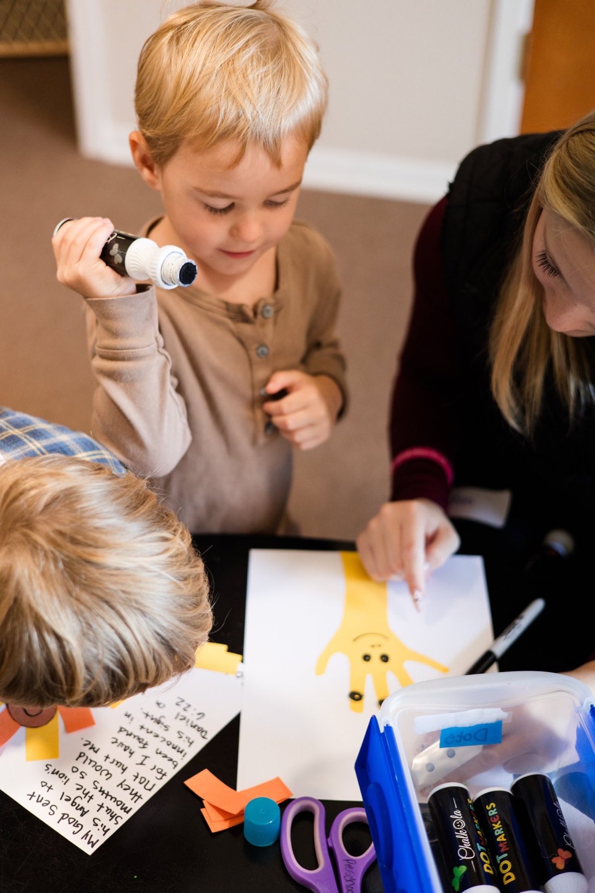 A preschool boy making a craft at a table with a volunteer