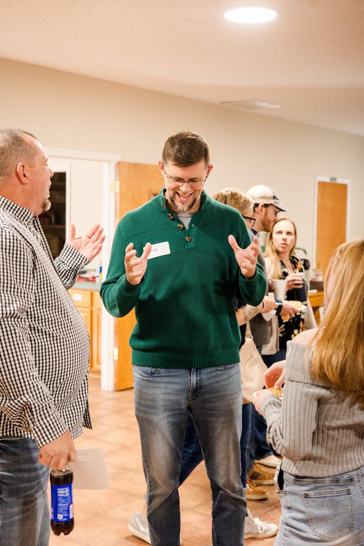 A man wearing a name tag laughs while talking with others in the welcome area.